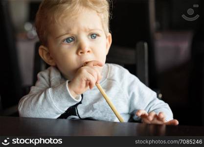 Baby boy sitting in high chair and plays with chopsticks at chinese restaurant.portrait horizontal.