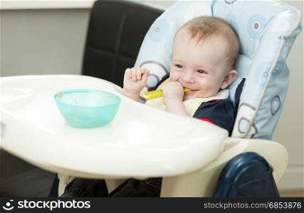 Baby boy sitting in highchair and playing with spoon and dish
