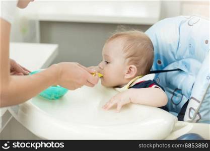 Baby boy sitting in highchair at kitchen and eating from spoon