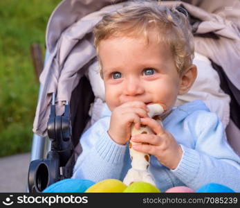 Baby boy sitting in the stroller happy playing with a toy.