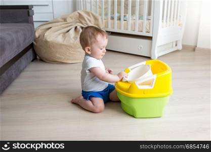 Baby boy sitting on floor and looking at chamber pot