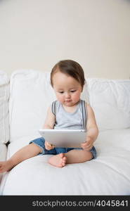 Baby boy sitting on sofa looking at digital tablet