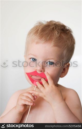 Baby boy with paper lips on a stick shows tongue