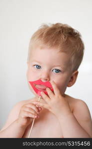 Baby boy with paper lips on a stick shows tongue