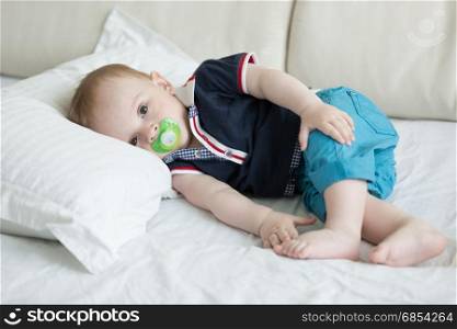 Baby boy with soother lying on pillow on sofa