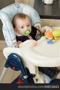 Baby boy with soother sitting in chair for feeding