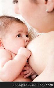 Baby breastfeeding on mothers breast drinking milk with antibodies. Cute eyes looking up while nursing.