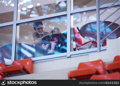 baby child in wheels and mom woman looking trough big modern window panel