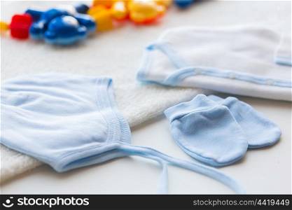 baby clothes and object concept - close up of white cardigan, mittens and hat with towel for newborn boy