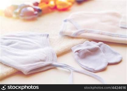 baby clothes and object concept - close up of white cardigan, mittens and hat with towel for newborn boy