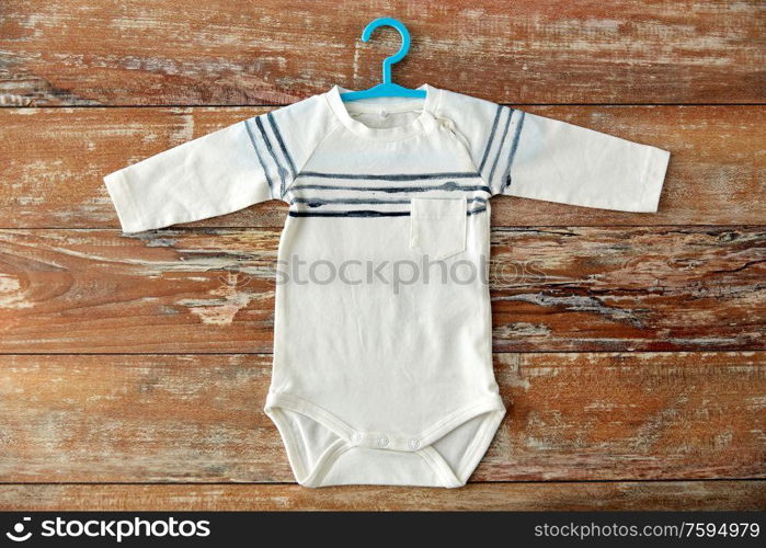 baby clothes, babyhood and clothing concept - bodysuit with hanger on wooden table. baby bodysuit with hanger on wooden table