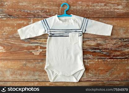 baby clothes, babyhood and clothing concept - bodysuit with hanger on wooden table. baby bodysuit with hanger on wooden table