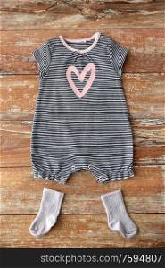 baby clothes, babyhood and clothing concept - striped bodysuit for girl with pink heart print and socks on wooden table. baby bodysuit and socks on wooden table