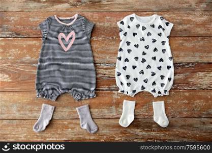 baby clothes, babyhood and clothing concept - two bodysuits and socks on wooden table. baby bodysuits and socks on wooden table