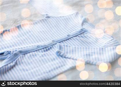 baby clothes, babyhood, motherhood and object concept - close up of blue bodysuit on towel for newborn boy with holidays lights