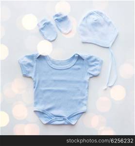 baby clothes, babyhood, motherhood and object concept - close up of blue bodysuit, hat and mittens for newborn boy on table