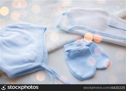 baby clothes, babyhood, motherhood and object concept - close up of white cardigan, mittens and hat with towel for newborn boy with holidays lights