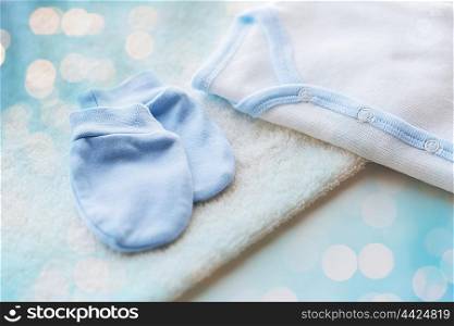 baby clothes, babyhood, motherhood and object concept - close up of white cardigan, mittens and towel for newborn boy