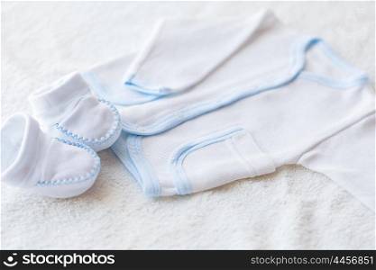 baby clothes, babyhood, motherhood and object concept - close up of white cardigan and bootees for newborn boy on towel