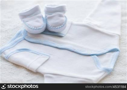 baby clothes, babyhood, motherhood and object concept - close up of white cardigan and bootees for newborn boy on towel
