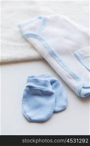 baby clothes, babyhood, motherhood and object concept - close up of white cardigan, mittens and towel for newborn boy