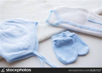 baby clothes, babyhood, motherhood and object concept - close up of white cardigan, mittens and hat with towel for newborn boy