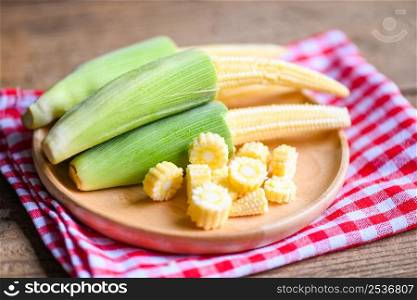 Baby corn on wooden plate, Fresh young baby corn for cooking health food, Close up raw organic baby corn on tablecloth background.