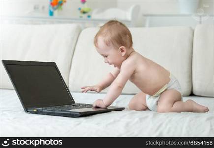 Baby crawling on bed and looking with interest on laptop