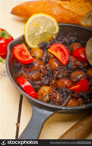 Baby cuttle fish roasted on iron skillet with tomatoes and onions over rustic wood table