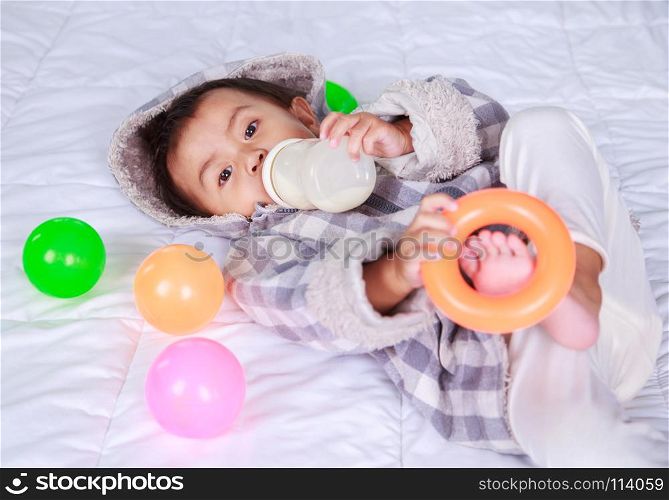 baby drinking milk with bottle on bed at home