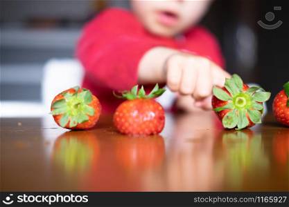 Baby exploring some fruits with his hand on a dark wooden table. Baby s hand manipulating different fruits on a wooden table