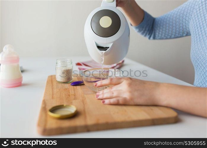 baby food and nutrition concept - mother hands preparing cereal and pouring water from kettle into bowl. mother pouring water into bowl for baby cereal