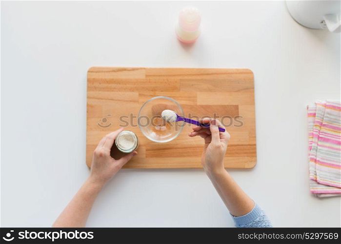 baby food and nutrition concept - mother hands with jar, spoon and bowl preparing cereal from powder. hands with spoon and jar making baby cereal