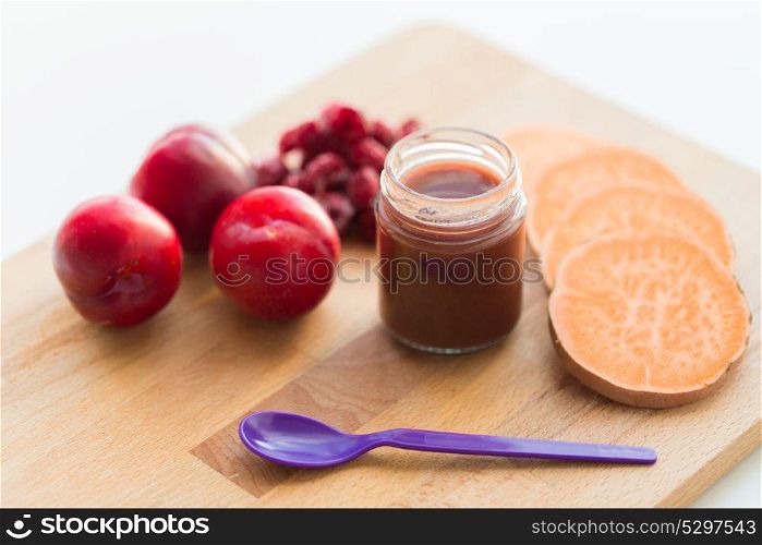 baby food, healthy eating and nutrition concept - fruit puree in glass jar with feeding spoon on wooden board. fruit puree or baby food in jar and feeding spoon
