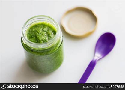 baby food, healthy eating and nutrition concept - glass jar of green vegetable or fruit puree and spoon on table. jar of vegetable puree or baby food and spoon