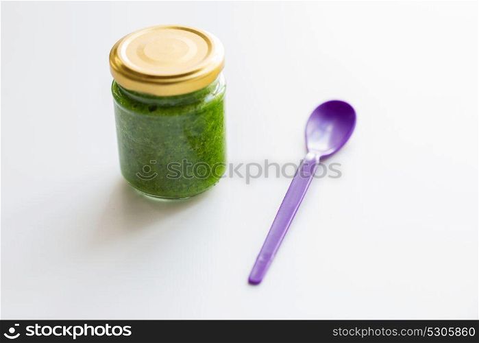 baby food, healthy eating and nutrition concept - glass jar of green vegetable or fruit puree and spoon on table. jar of vegetable puree or baby food and spoon