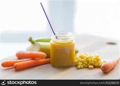 baby food, healthy eating and nutrition concept - glass jar puree with carrot, banana and corn on wooden board. puree or baby food with fruits and vegetables