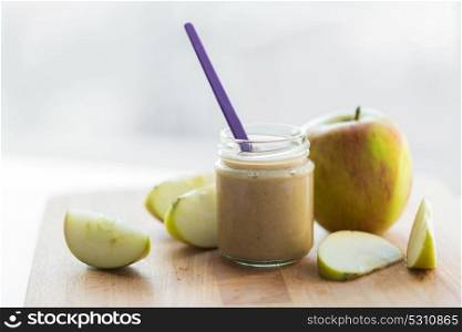 baby food, healthy eating and nutrition concept - glass jar with apple fruit puree on wooden board. jar with apple fruit puree or baby food on table
