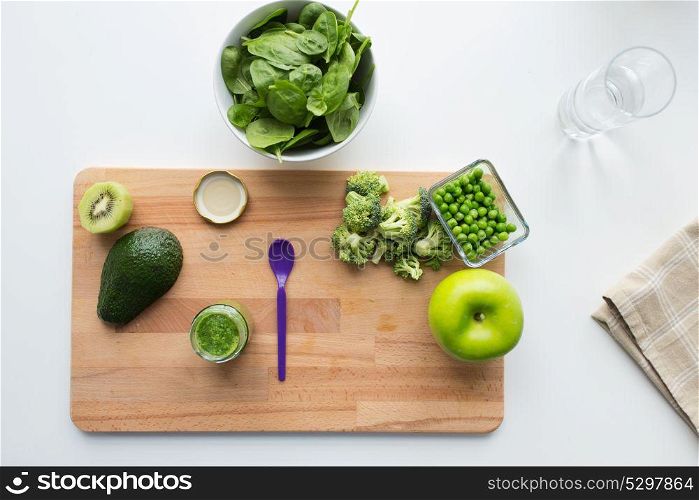 baby food, healthy eating and nutrition concept - glass jar with green vegetable puree, feeding spoon and fruits on wooden board. vegetable puree or baby food and fruits on board