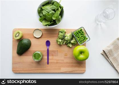 baby food, healthy eating and nutrition concept - glass jar with green vegetable puree, feeding spoon and fruits on wooden board. vegetable puree or baby food and fruits on board