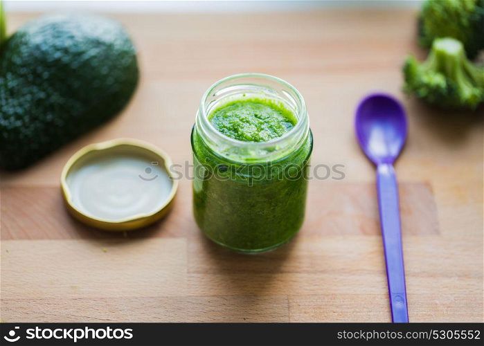 baby food, healthy eating and nutrition concept - glass jar with green vegetable puree on wooden cutting board. jar with puree or baby food on wooden board