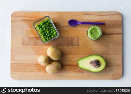 baby food, healthy eating and nutrition concept - glass jar with green vegetable puree and feeding spoon on wooden board. vegetable puree or baby food on wooden board