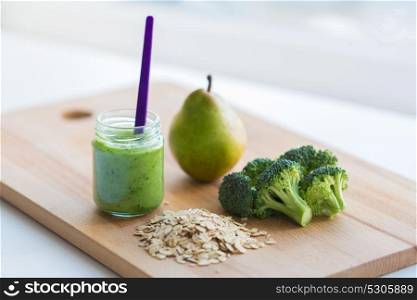 baby food, healthy eating and nutrition concept - glass jar with green vegetarian puree on wooden cutting board. jar with puree or baby food on wooden board