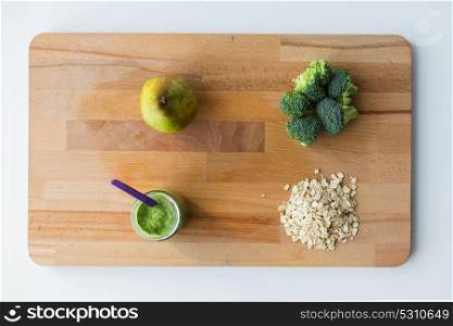 baby food, healthy eating and nutrition concept - glass jar with green vegetable puree, pear, broccoli and oatmeal on wooden cutting board. jar with puree or baby food on wooden board