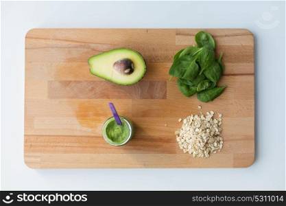 baby food, healthy eating and nutrition concept - glass jar with green vegetable puree and oatmeal on wooden cutting board. jar with puree or baby food on wooden board