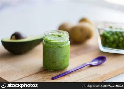 baby food, healthy eating and nutrition concept - glass jar with green vegetarian puree on wooden cutting board. jar with puree or baby food on wooden board