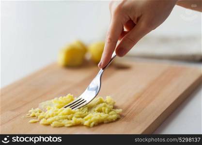 baby food, healthy eating and nutrition concept - hand with fork making mashed potato on wooden board. hand with fork making mashed potato on board