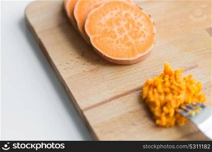 baby food, healthy eating and nutrition concept - hand with fork making mashed batata on wooden board. hand with fork making mashed batata on board