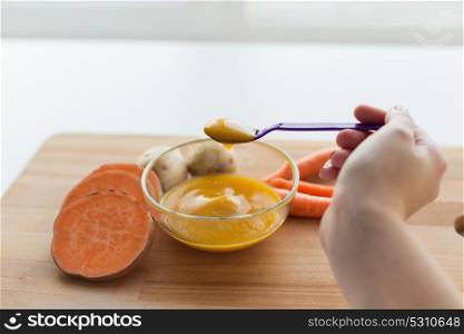 baby food, healthy eating and nutrition concept - hand with vegetable puree in feeding spoon. hand with vegetable puree or baby food in spoon