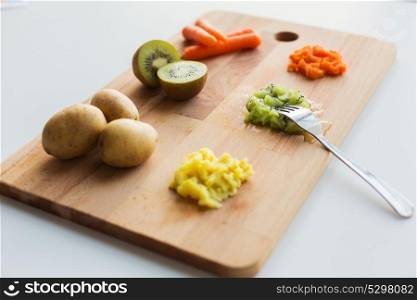baby food, healthy eating and nutrition concept - mashed fruits and vegetables with forks on wooden cutting board. mashed fruits and vegetables with forks on board